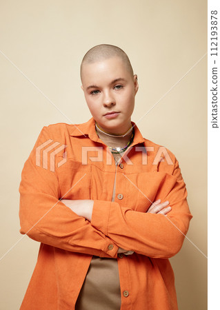 Portrait of bald young woman wearing bright orange jacket posing in studio with confidence Portrait of bald young woman wearing bright orange jacket posing in studio with confidence 112193878