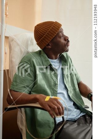 Vertical side view portrait of African American man wearing beanie hat while receiving IV treatment in clinic Vertical side view portrait of African American man wearing beanie hat while receiving IV treatment in clinic 112193948