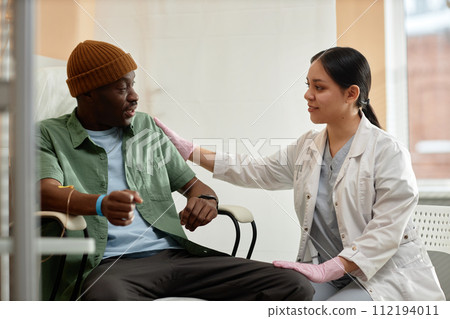 Side view portrait of smiling female doctor comforting patient receiving IV treatment in clinic 112194011