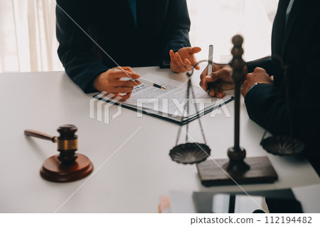 Justice and Law concept. Legal counsel presents to the client a signed contract with gavel and legal law or legal having team meeting at law firm in background Justice and Law concept. Legal counsel presents to the client a signed contract with gavel and legal law or legal having team meeting at law firm in background 112194482