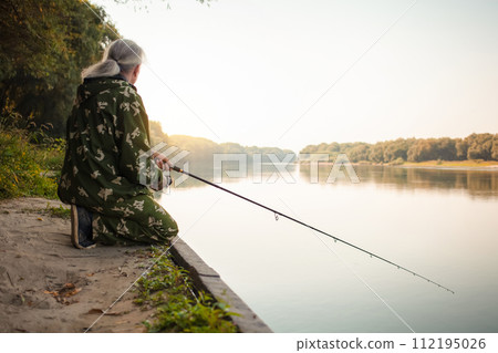 senior concept. pensioner fishes on the river in his spare time. A useful hobby, outdoor activities in old age. copy space. dawn senior concept. pensioner fishes on the river in his spare time. A useful hobby, outdoor activities in old age. copy space. dawn 112195026