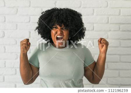 Angry african american woman screaming on brick background. Bad aggressive emotions and premenstrual syndrome or pms concept 112196239