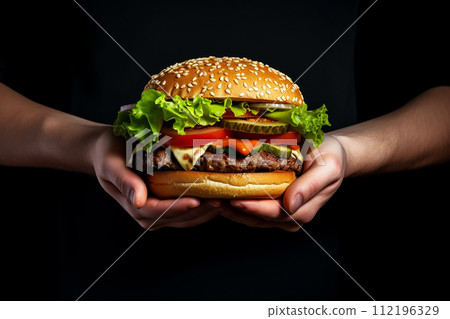Two hands holding a juicy burger with lettuce, cheese, and tomatoes. 112196329