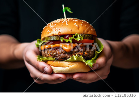 Two hands holding a juicy burger with lettuce, cheese, and tomatoes. 112196330
