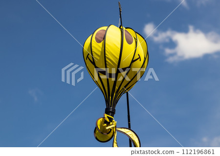 Smiling yellow balloon against a blue sky with a small white cloud 112196861