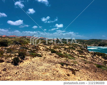 Houses with orange roofs line the top of a rugged cliff under a sky with few clouds. Houses with orange roofs line the top of a rugged cliff under a sky with few clouds. 112196889