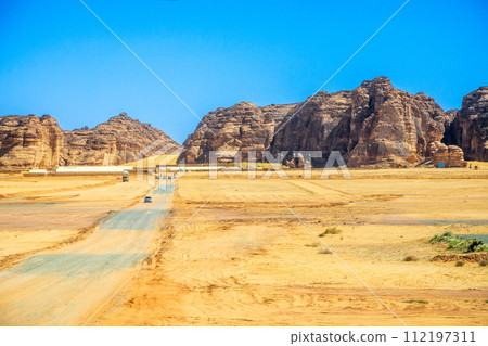 Desert sand landscape with mountains in the background and road with cars, near Al Ula, Saudi Arabia 112197311