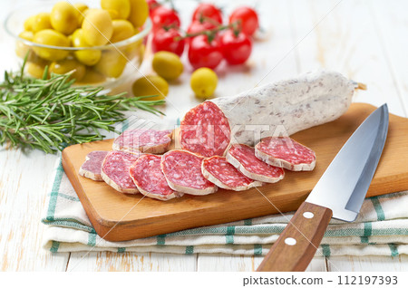 Traditional Spanish fuet spicy pork dry cured salami sausage with rosemary and baguet on a wooden table. 112197393