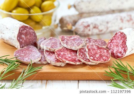 Spanish Fuet sausage salami with rosemary and olives on a wooden cutting board. 112197396