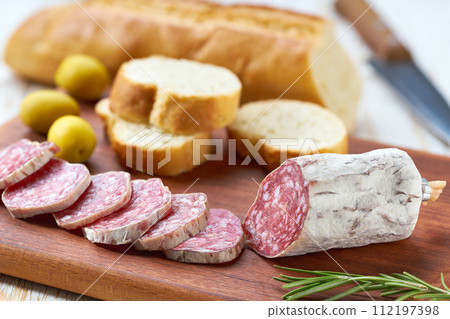Spanish Fuet sausage salami with rosemary and french baguette on a cutting board. 112197398