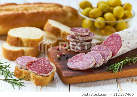 Spanish dried sausage with slices on a wooden board and next to olives and bread. Spanish dried sausage with slices on a wooden board and next to olives and bread. 112197400
