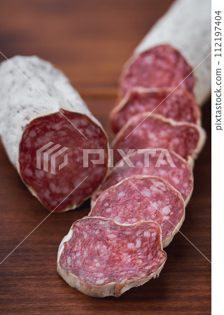 traditional Spanish salami fuet sausage or dry sausage cut in slices in a kitchen table. 112197404
