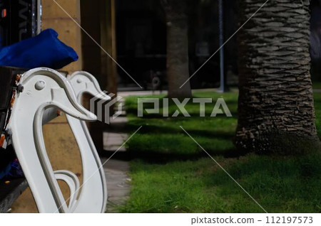 A bench with two white swans on it is in a park A bench with two white swans on it is in a park 112197573