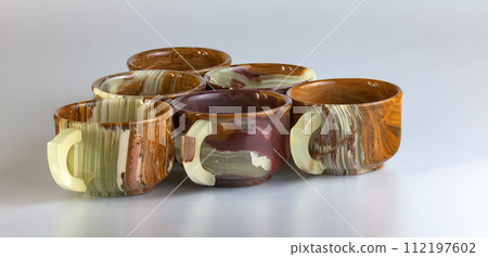 Empty cups made of multi-colored onyx in yellow-orange tones on a white background. Empty cups made of multi-colored onyx in yellow-orange tones on a white background. 112197602