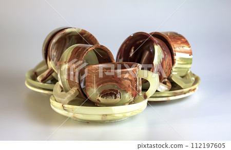 Empty cups made of multi-colored onyx in yellow-orange tones on a white background. 112197605