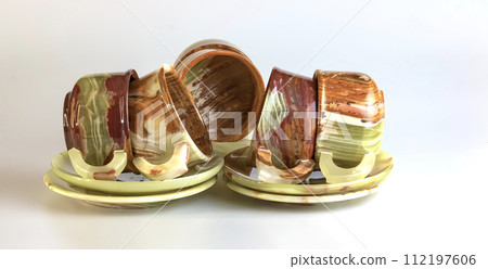Empty cups made of multi-colored onyx in yellow-orange tones on a white background. 112197606