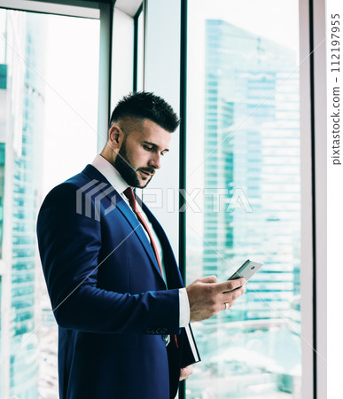 Thoughtful adult executive man using smartphone in office Thoughtful adult executive man using smartphone in office 112197955