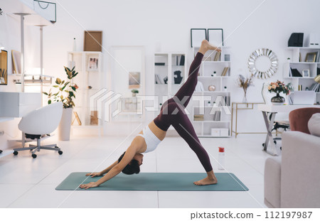 Slim woman doing single legged downward facing dog yoga on mat Slim woman doing single legged downward facing dog yoga on mat 112197987