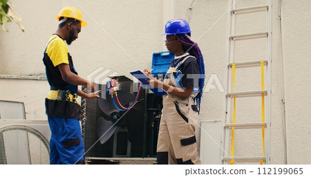 Diverse team of capable electricians brainstorming possible ways to repair damaged outdoor hvac system. Seasoned wiremen colleagues commissioned to fix broken air conditioner Diverse team of capable electricians brainstorming possible ways to repair damaged outdoor hvac system. Seasoned wiremen colleagues commissioned to fix broken air conditioner 112199065
