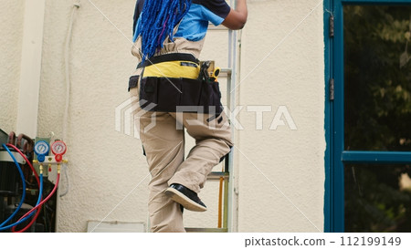 African american specialist in professional uniform with technical equipment climbing folding ladder to do maintenance on rooftop air conditioner. Trained engineer commissioned to checkup on condenser African american specialist in professional uniform with technical equipment climbing folding ladder to do maintenance on rooftop air conditioner. Trained engineer commissioned to checkup on condenser 112199149