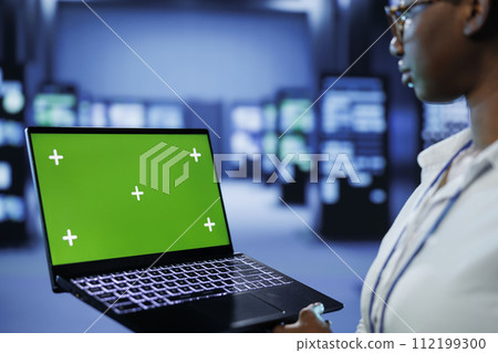 Programmer in server room uses green screen laptop to future proof network from downtimes and unexpected system failures. Tech support with mockup device ensures increased data security Programmer in server room uses green screen laptop to future proof network from downtimes and unexpected system failures. Tech support with mockup device ensures increased data security 112199300