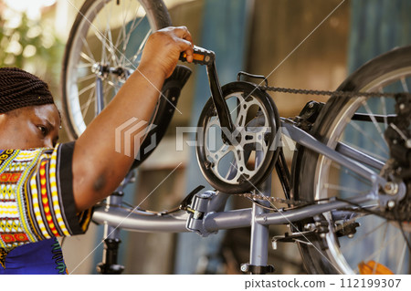 Passionate sports-loving black woman diligently inspecting and repairing bike pedals and chains. Active african american female cyclist making annual adjustments to modern bicycle. 112199307