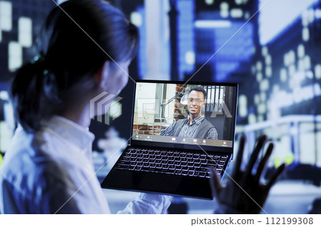 Asian man in videocall with coworker while strolling around city streets at night, giving him work updates. Person using laptop to show colleague surroundings in nighttime urban environment Asian man in videocall with coworker while strolling around city streets at night, giving him work updates. Person using laptop to show colleague surroundings in nighttime urban environment 112199308