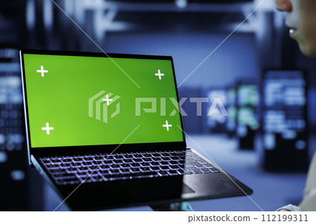 IT consultant with chroma key laptop between server hub clusters providing processing resources for businesses worldwide. Worker uses isolated screen device to fix data center mainframes IT consultant with chroma key laptop between server hub clusters providing processing resources for businesses worldwide. Worker uses isolated screen device to fix data center mainframes 112199311