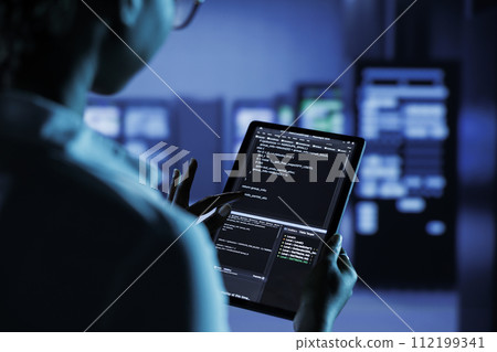 Close up of skilled worker running code and programming on laptop, troubleshooting and upgrading high tech facility designed to accommodate multiple clusters of fully operational server units Close up of skilled worker running code and programming on laptop, troubleshooting and upgrading high tech facility designed to accommodate multiple clusters of fully operational server units 112199341