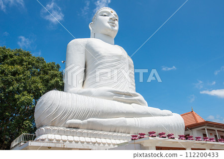 The white giant Buddha statue in Sri Maha Bodhi Viharaya located on the top of small hill in Kandy city, Sri Lanka. This beautiful white statue can be seen from the entire city of Kandy. 112200433