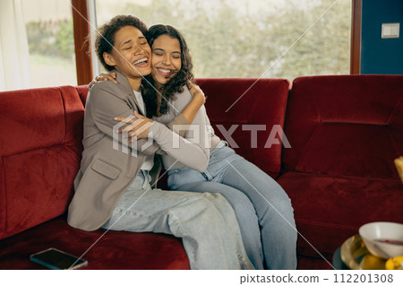 Smiling female friends hugging and enjoy time spent together while sitting on sofa during home party Smiling female friends hugging and enjoy time spent together while sitting on sofa during home party 112201308