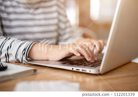 A close-up shot of a woman working on her laptop computer at her desk, typing on laptop keyboard. 112201339