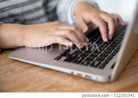 A close-up shot of a woman working on her laptop computer at her desk, typing on laptop keyboard. 112201341