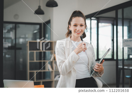 Engaging and friendly businesswoman holding a tablet, ready to start a productive meeting in a bright office space. Engaging and friendly businesswoman holding a tablet, ready to start a productive meeting in a bright office space. 112201638