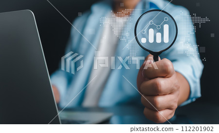 Businessman hand holding magnifier and zooming at candlesticks bar chart of stock market data, Finance and investment data search concept, Stock market analyzing, Stock information search. 112201902
