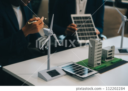 Two Young Engineers Expertise in Solar Cell Installation Meetings and Discussion in The Job. Planning to Install Solar Photovoltaic Panels on Roof Top in The Office Room with Factory Building Plan. 112202284
