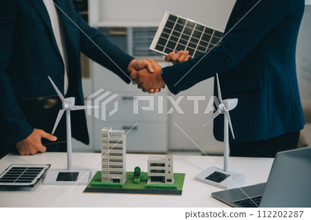 Two Young Engineers Expertise in Solar Cell Installation Meetings and Discussion in The Job. Planning to Install Solar Photovoltaic Panels on Roof Top in The Office Room with Factory Building Plan. 112202287