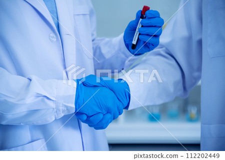 Two asian scientist men team partner shake hands together. Men researcher holding chemistry science tube experiment biotech antibody sample in laboratory. Close up hand corporate coworker partnership 112202449