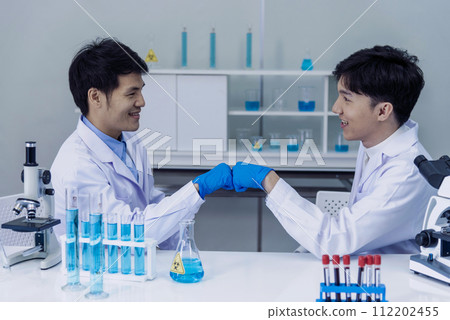 Two asian scientist men fist bump team partner shake hands together. Teamwork Men science chemistry research working success in laboratory. Close up hand pharmaceutical science corporate partnership 112202455