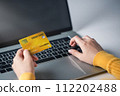 A woman holds a credit card and pays for an online purchase. 112202488