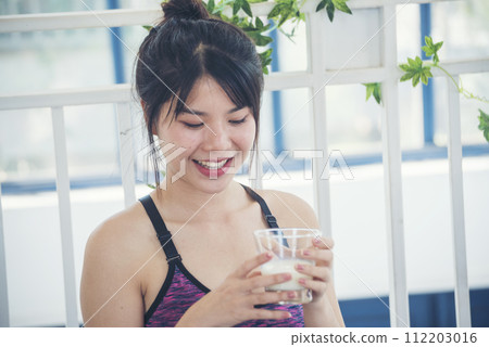 Women hands holding white glass of milk pouring from bottle. Asian women smile laugh look at camera health care home fitness lifestyle. Beautiful female drinking fresh milk low-fat dairy free lactose 112203016