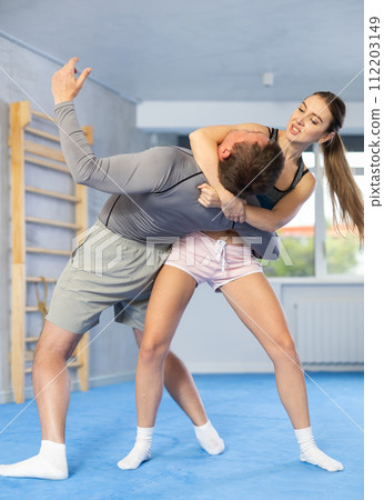 Young woman learning to do power grab on an opponent neck during self-defense training at gym Young woman learning to do power grab on an opponent neck during self-defense training at gym 112203149