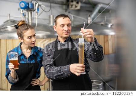 Couple of brewmasters using hydrometer to check alcoholic content in beer Couple of brewmasters using hydrometer to check alcoholic content in beer 112203154