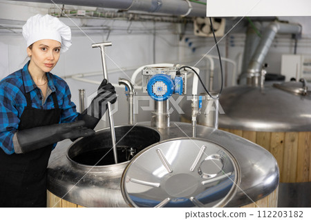 Woman brewmaster standing at opened tank in beer factory 112203182