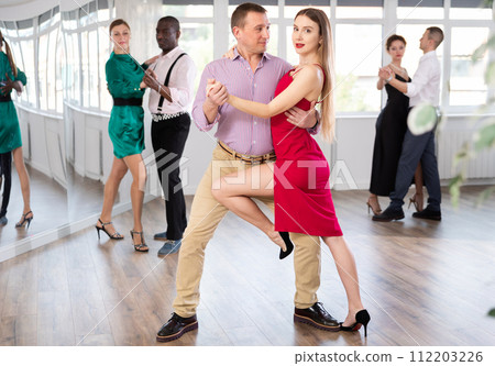 Elegant couple performs an expressive tango in bright, modern dance studio during group class Elegant couple performs an expressive tango in bright, modern dance studio during group class 112203226