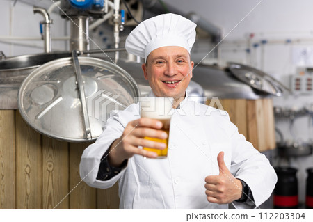 Portrait of brewer who is standing with glass of beer on his workplace in brew-house Portrait of brewer who is standing with glass of beer on his workplace in brew-house 112203304