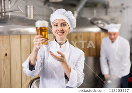 Positive woman brewer presenting glass of fresh beer 112203317
