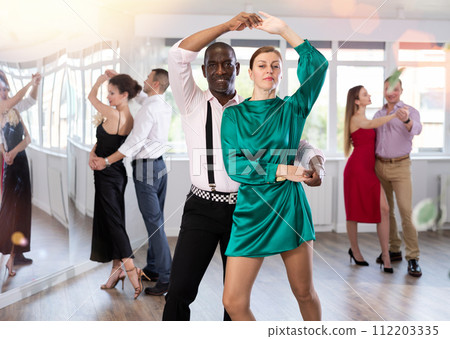 Woman with African man dancing waltz in couple during lesson at studio 112203335