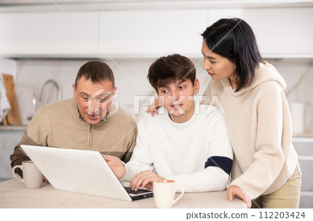 Friendly family watches something together on the Internet or video chats via laptop 112203424