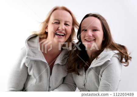 a woman and a girl hugging leaning their cheeks against each other look into the frame pull lips for kiss mom and daughter on white background identical clothes close eyes from pleasure tenderness joy 112203489